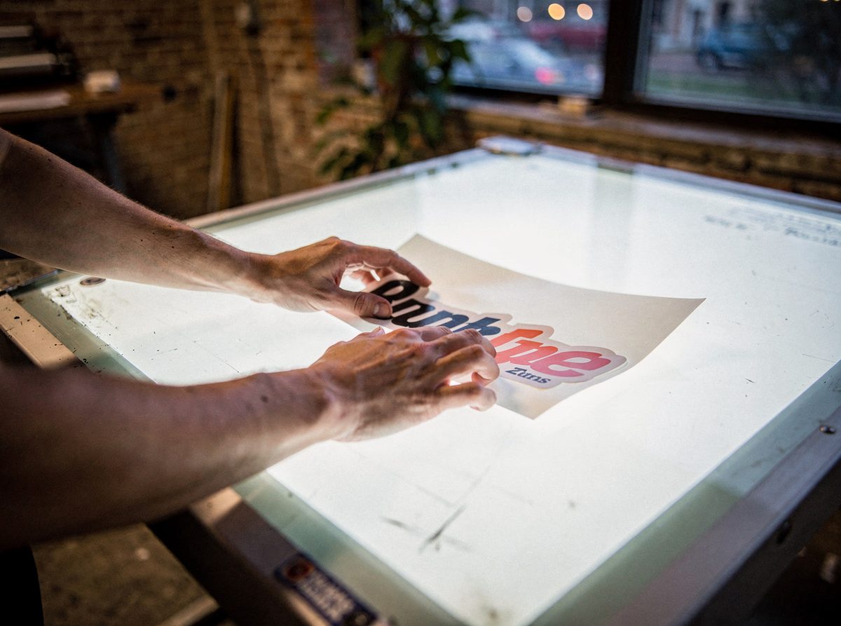 Hands positioning a die-cut vinyl logo proof on a light table